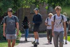 A group of young men walk and skateboard on DU's campus on a nice day.